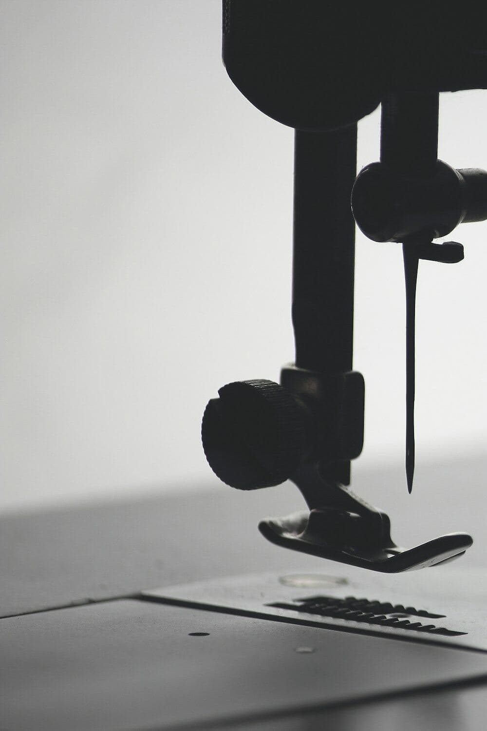 Tall portrait crop of a sewing machine needle and presser foot poised over the stitch plate